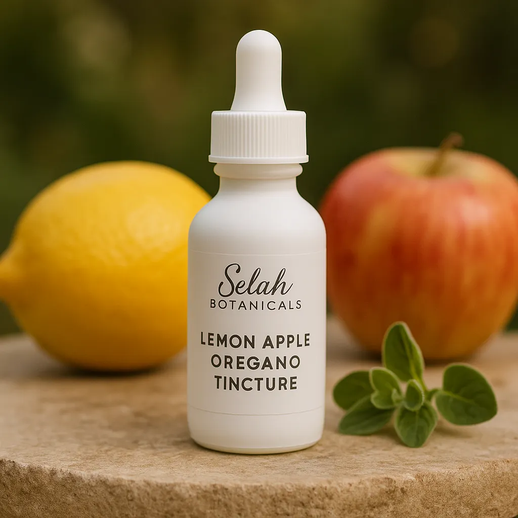 A white dropper bottle labeled "Selah Botanicals Lemon Apple Oregano Tincture" sits on a stone surface with a lemon, an apple, and oregano leaves in the background.